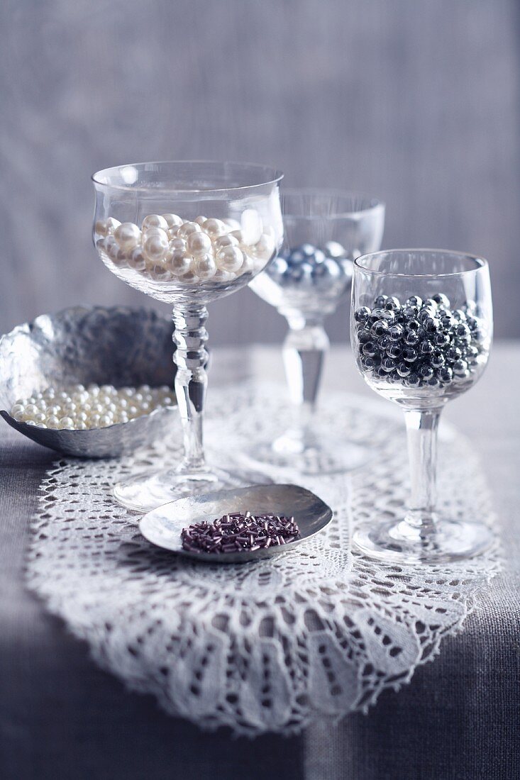 Craft beads in silver dishes and wine glasses on lace doily