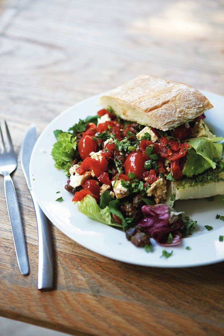 Mediterranean salad combination, overflowing from a ciabatta sandwich, on a plate