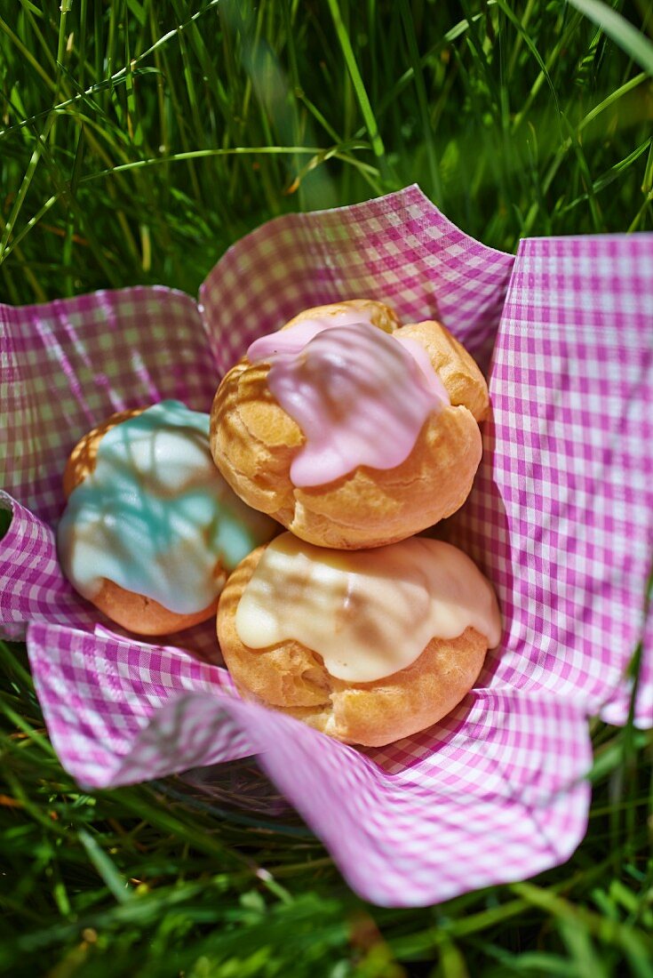 Choux pastries with colourful glacé icing on a napkin in the grass