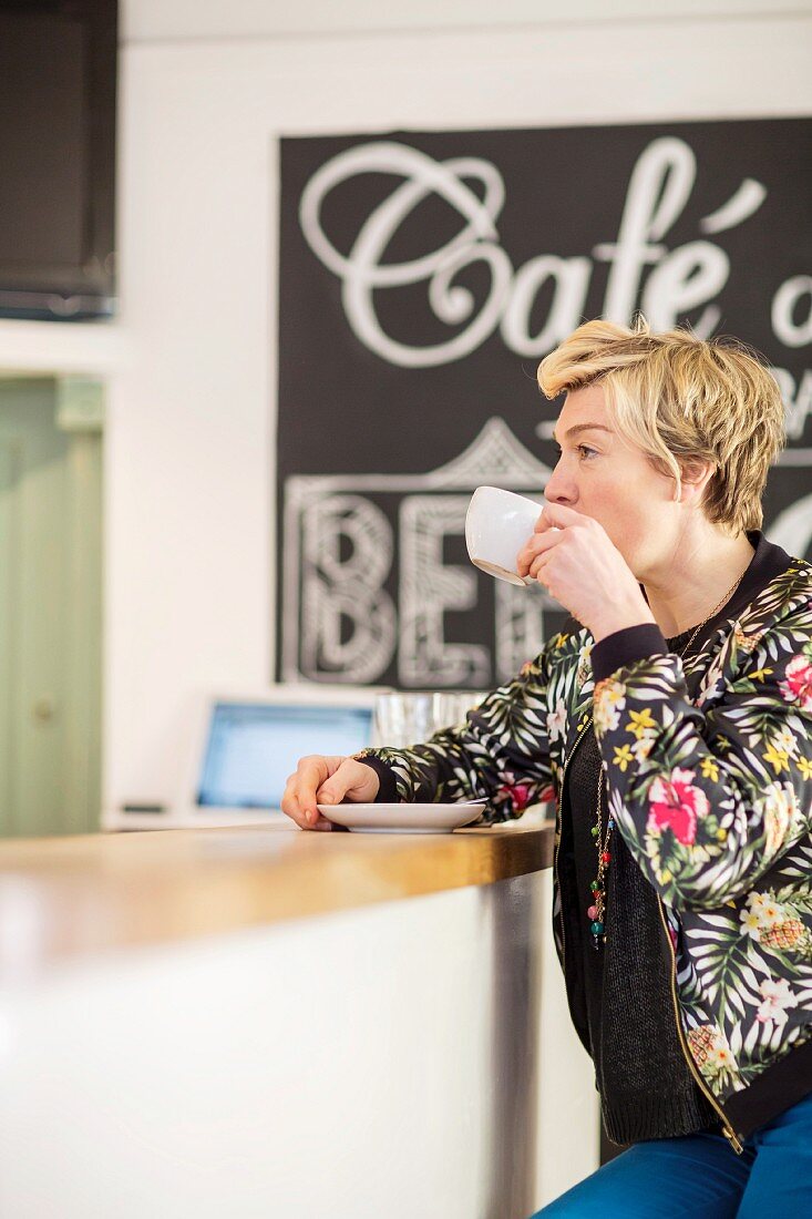 A woman sitting at the counter in a café, drinking coffee