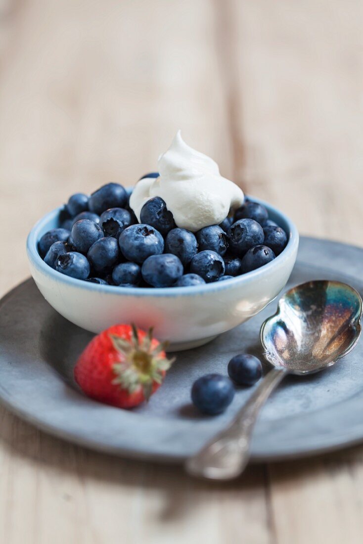 Fresh Blueberries with Whipped Cream in a Bowl; Strawberry and Spoon