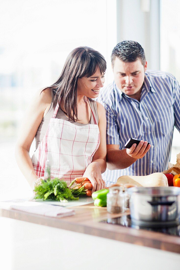 A couple cooking together in the kitchen and looking at a smartphone