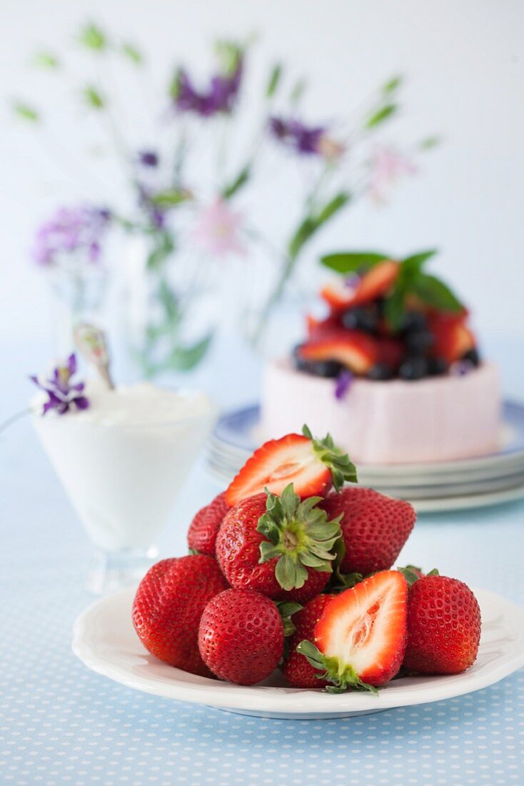 Frische Erdbeeren vor Joghurttorte mit Erdbeeren und Heidelbeeren