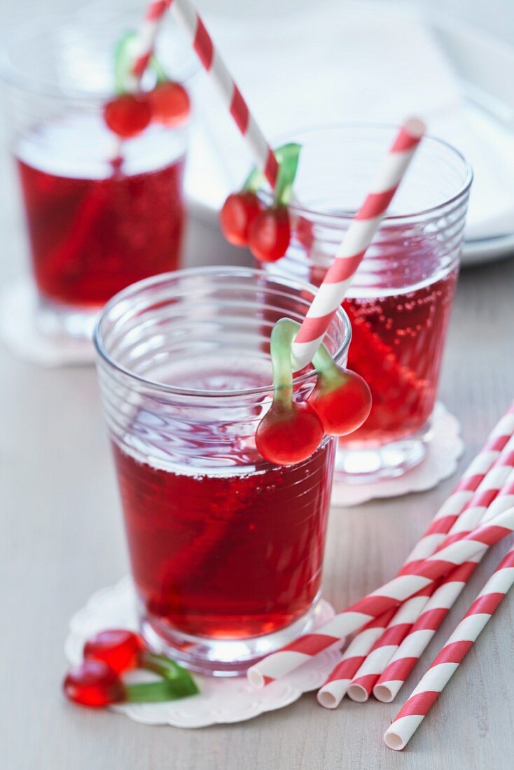 Cherry juice spritzer in glasses with straws decorated with cherry jelly sweets