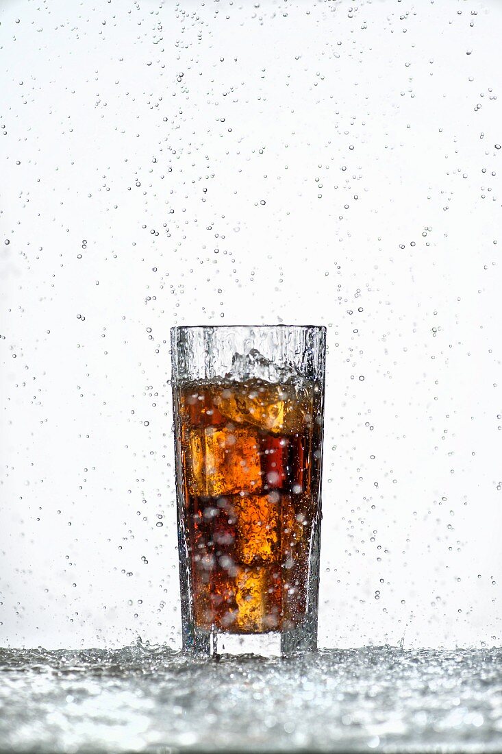 A glass of cola with ice cubes in a rain shower