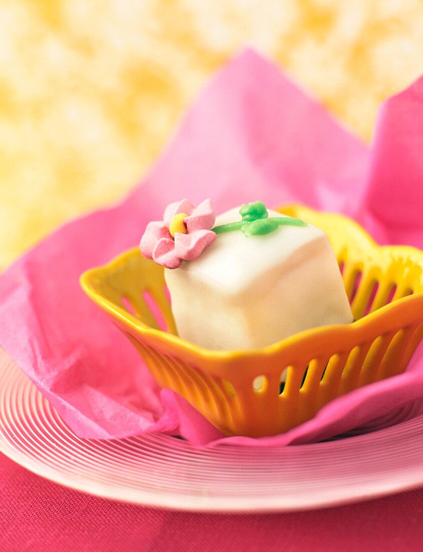 Petit Four in einem gelben Schälchen auf rosa Papier