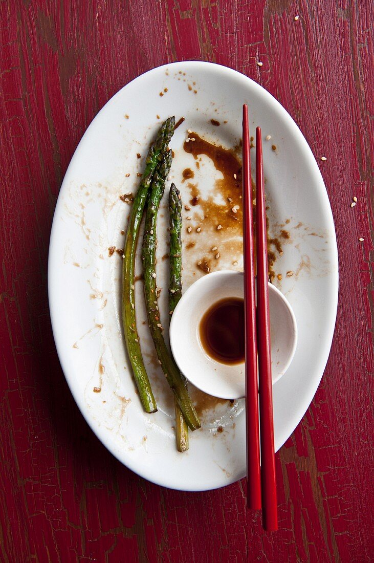 Remains of a meal of fried asparagus and soy sauce on a plate with chopsticks