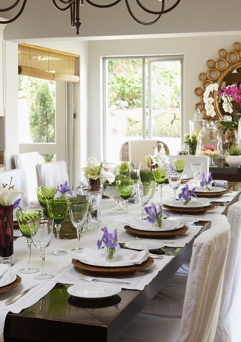 Festlich gedeckte Tafel mit grünen Weingläsern und Deko aus lila Irisblüten, weissen Lilien und Kräutertöpfen