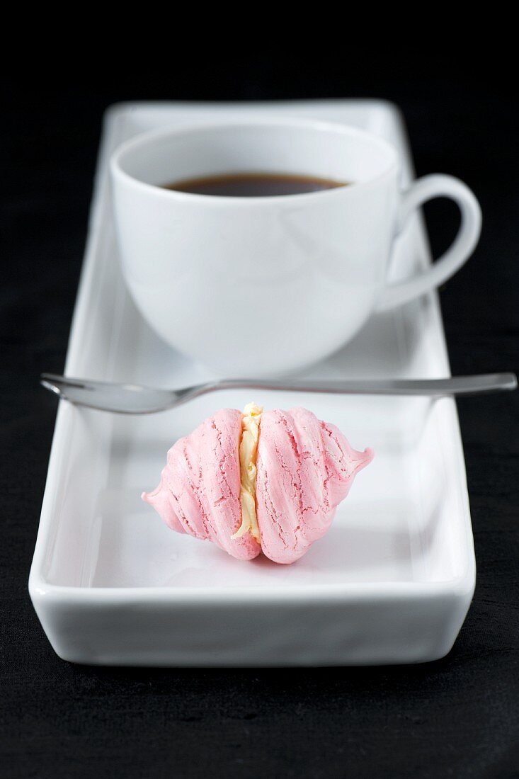Tasse Kaffee mit kleinem rosa Baiserplätzchen