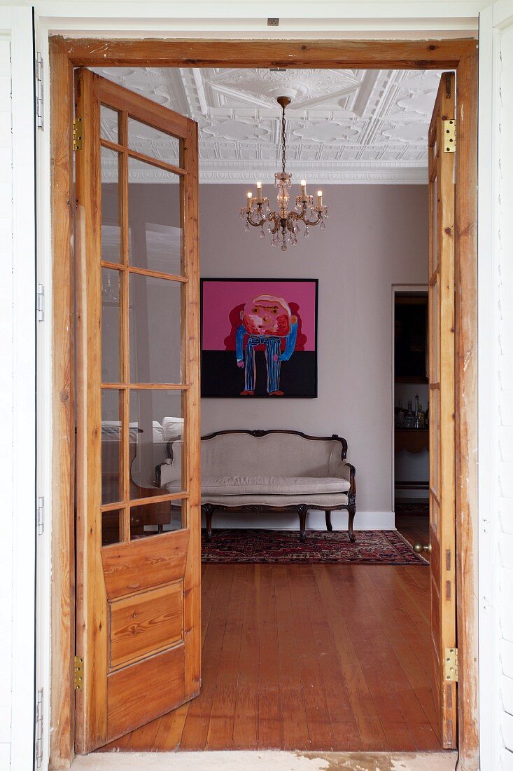 View though open door of Rococo-style bench below modern picture on wall