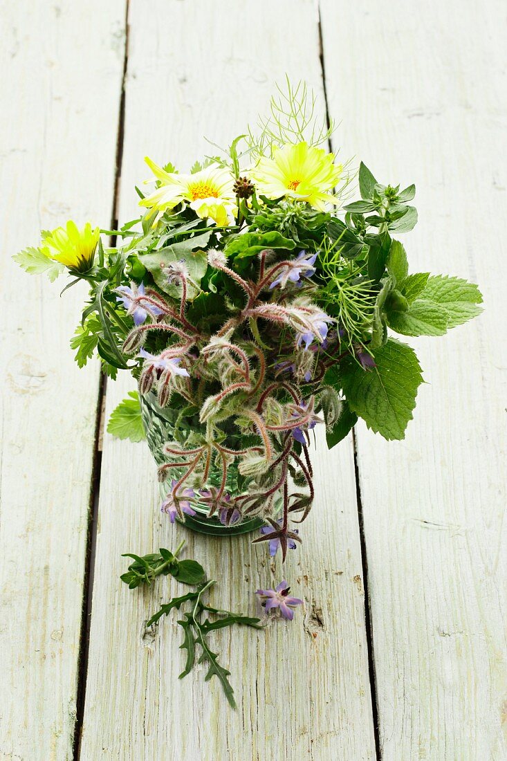A bunch of herbs with borage and marigolds in a glass of water