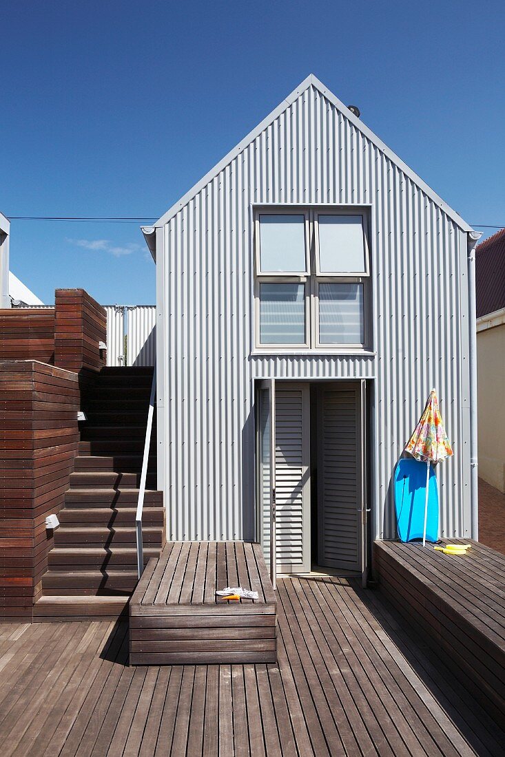 Wooden terrace with lounger platform in front of South African beach house with sheet metal, industrial-style facade