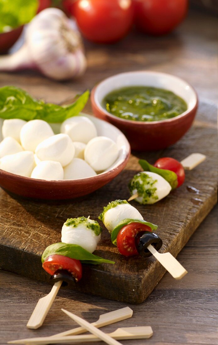 Skewers with mozzarella balls, tomatoes, basil, olives and pesto