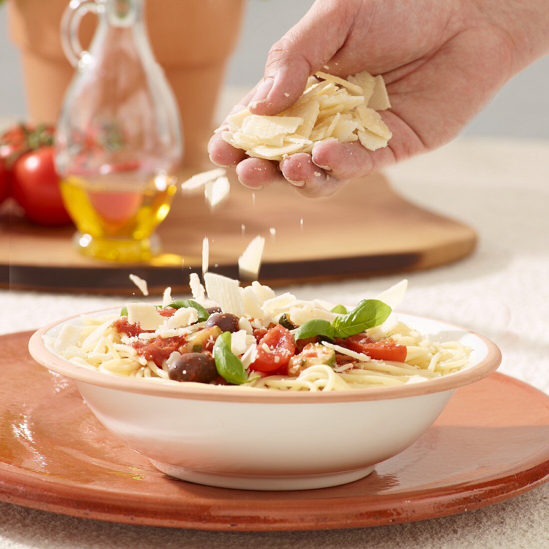 A spaghetti dish being sprinkled with parmesan