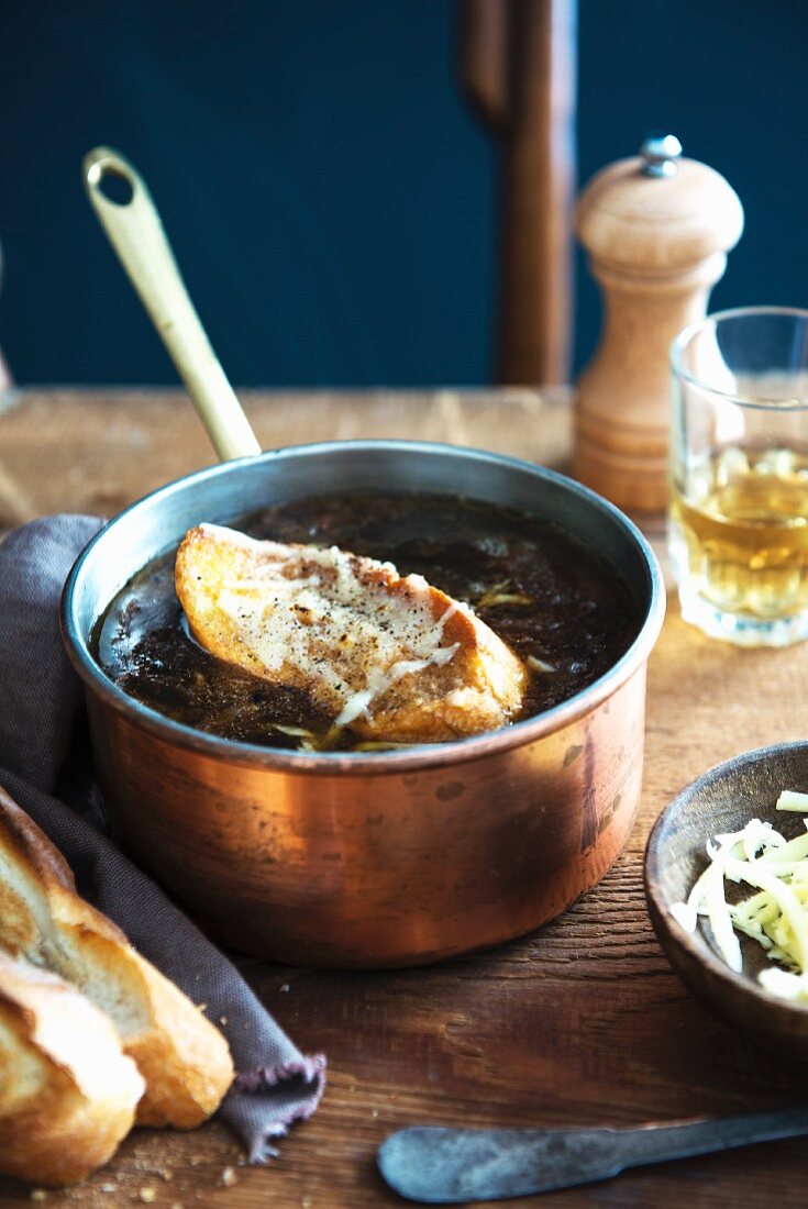 French onion soup with a slice of baguette in a copper pan