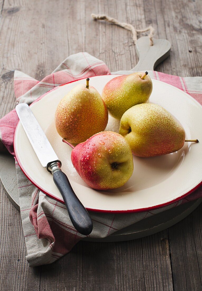 Four pears with water droplets and a knife on a plate