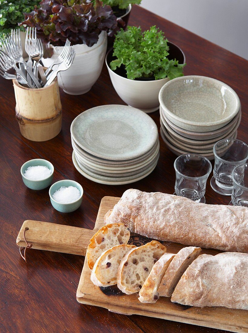 Tisch mit Ciabatta Brot auf Holz brett, gestapeltes Geschirr und Gläser
