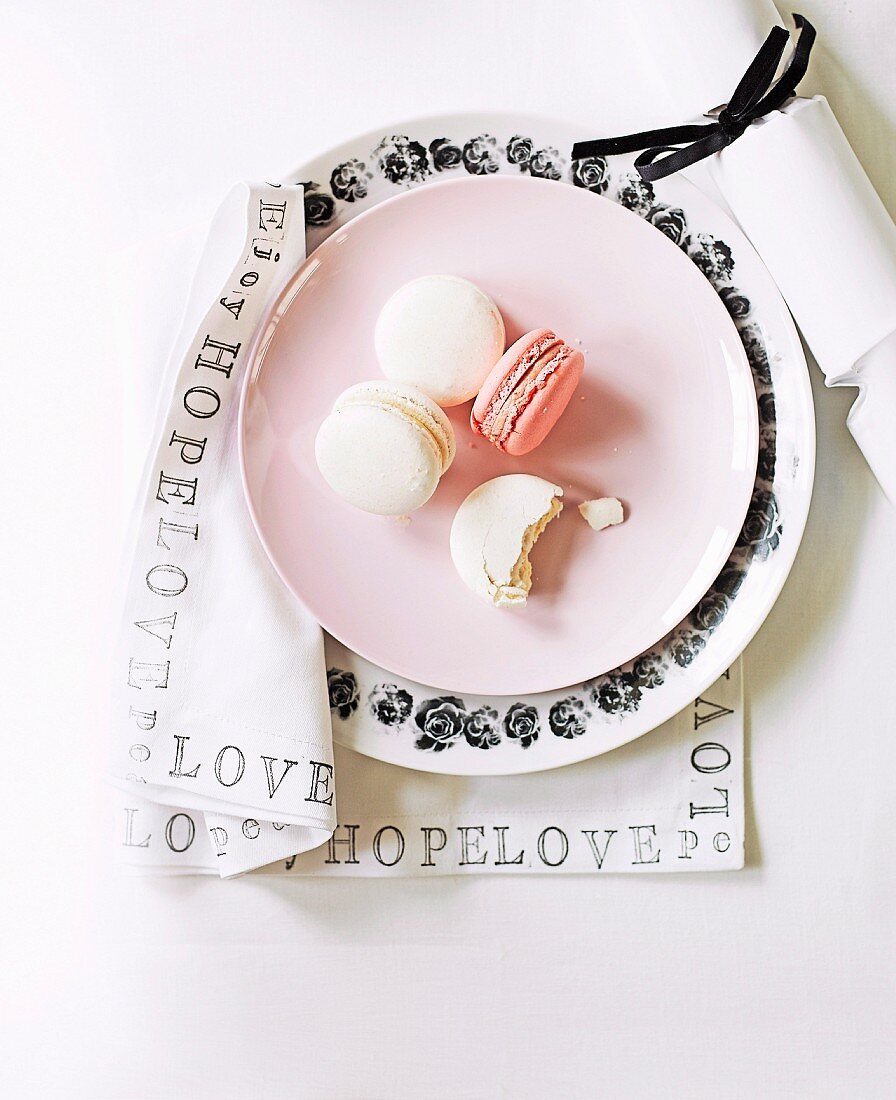 Place setting with macaroons on pink dessert plate and black and white floral plate on napkin printed with black lettering