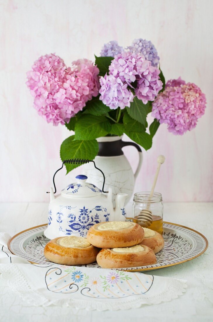 Vatrushka (Quarktasche, Russland), Teekanne, Honigglas und Hortensienstrauss