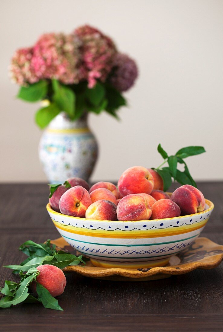 Pfirsiche in einer Schüssel vor Blumenvase