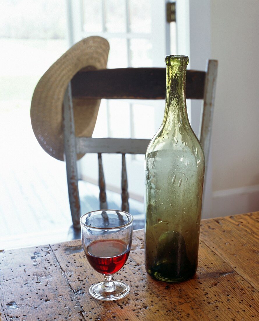 Glas Rotwein & leere Weinflasche auf altem Holztisch
