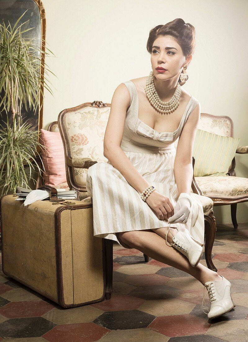 Woman wearing vintage, retro clothing sitting on chair waiting with suitcase