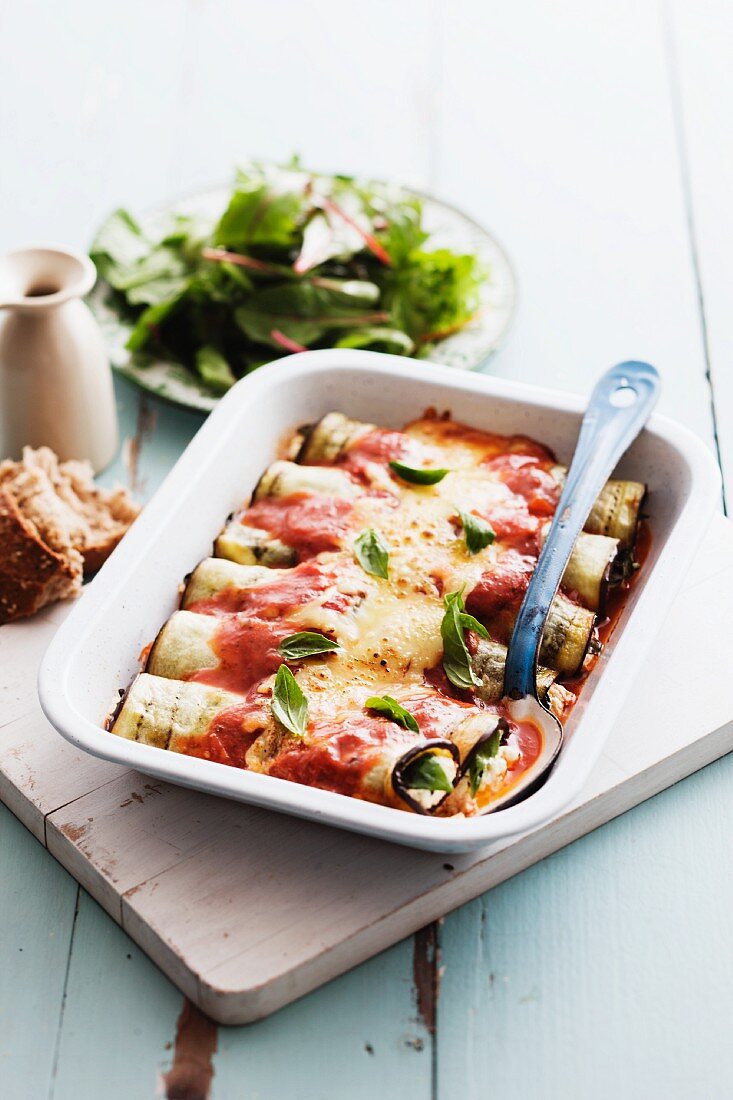 Slices of aubergine, stuffed and rolled, topped with cheese and baked