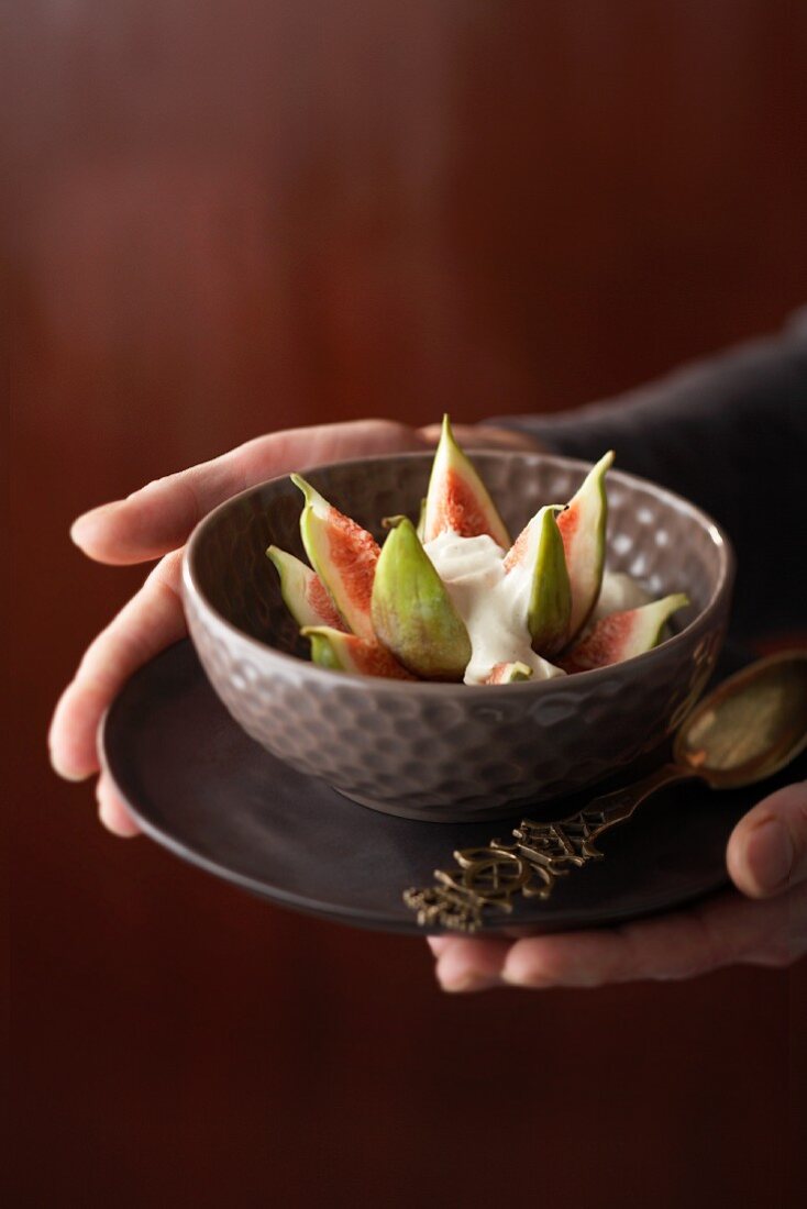 Hands holding a bowl of figs with cinnamon and mascarpone cream