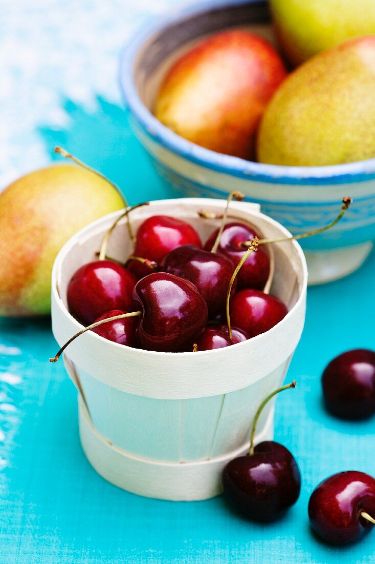 Cherries in a punnet in front of a bowl of pears