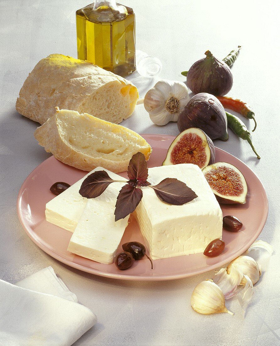 Piece of feta on plate with figs, olives & white bread