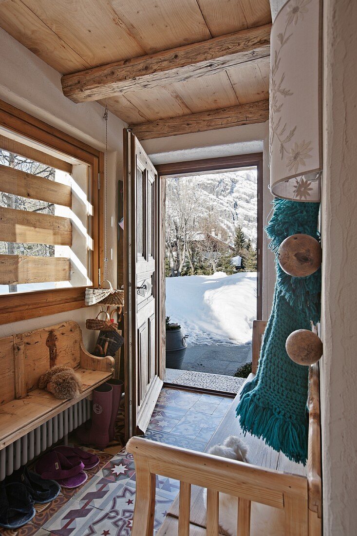 Offene Haustür im Eingangsbereich einer Holzhütte mit Blick auf verschneite Landschaft