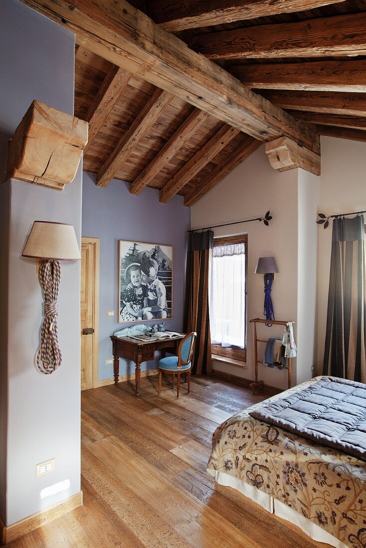 Attic bedroom with rustic wood-beamed ceiling and walls painted white and lavender grey