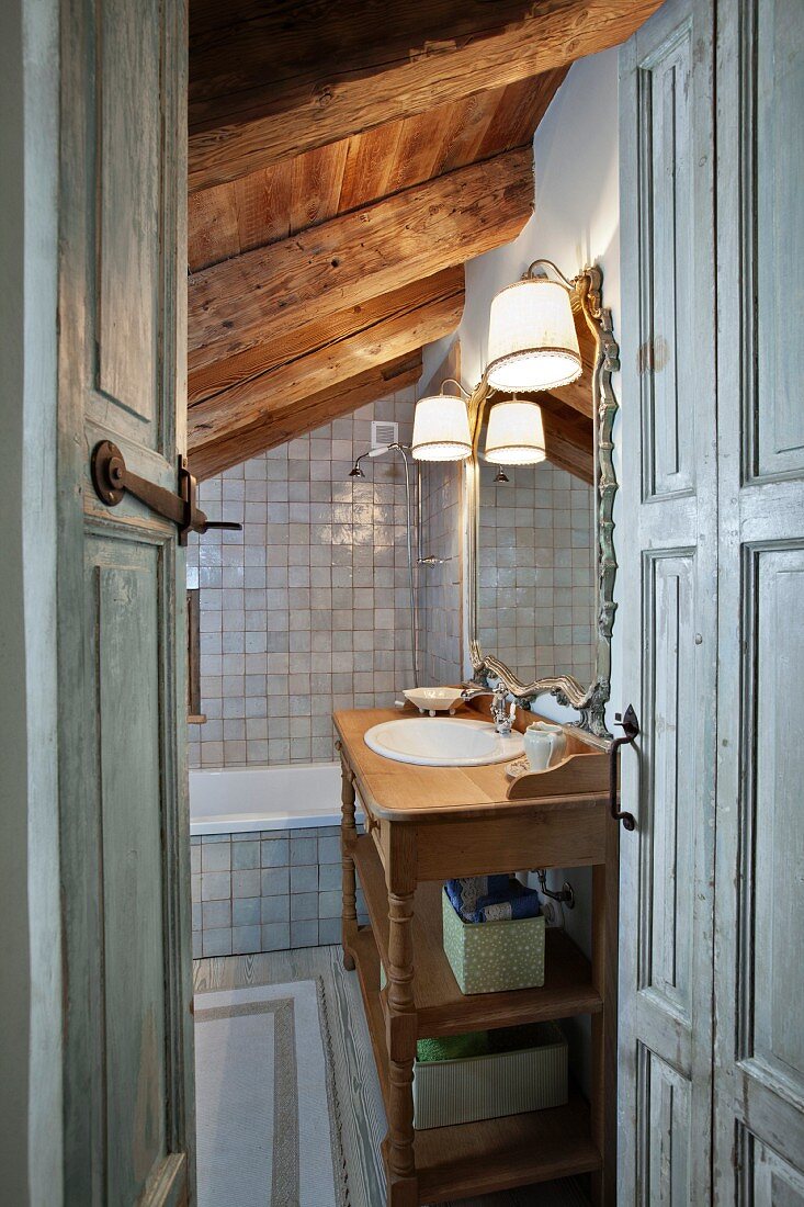 Blick in grau gefliestes Bad mit rustikalem Holz-Waschtisch, Spiegel und Wandleuchten