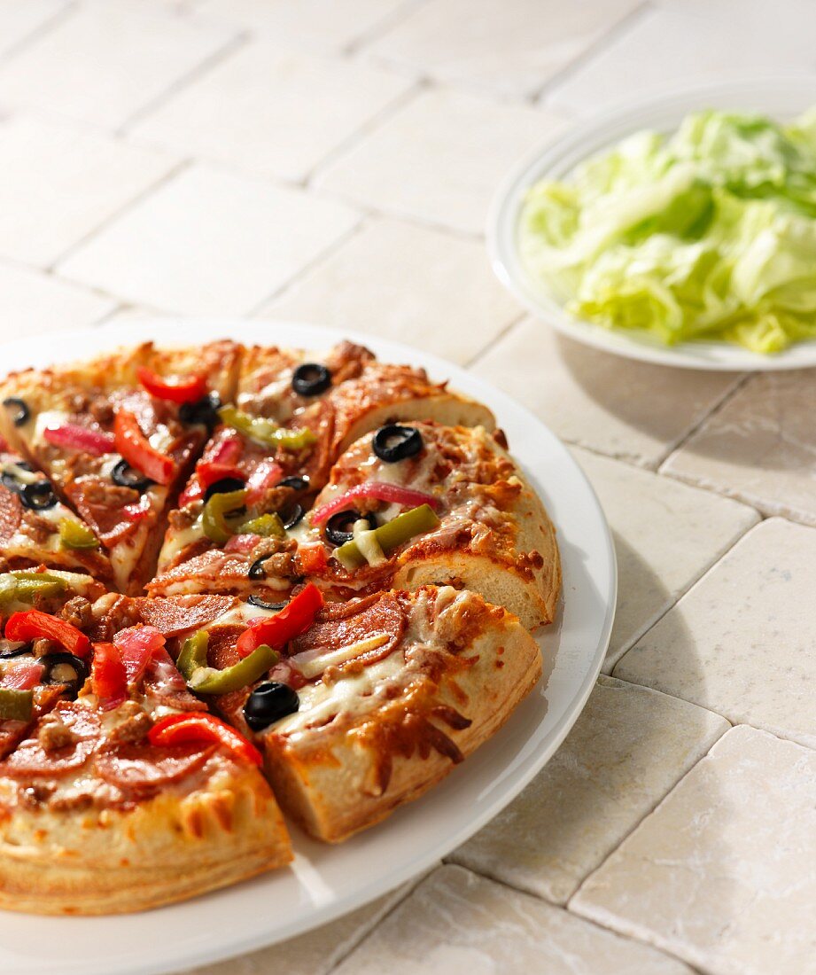 Pizza mit Salami, Paprika, Käse und Oliven, als Beilage Kopfsalat