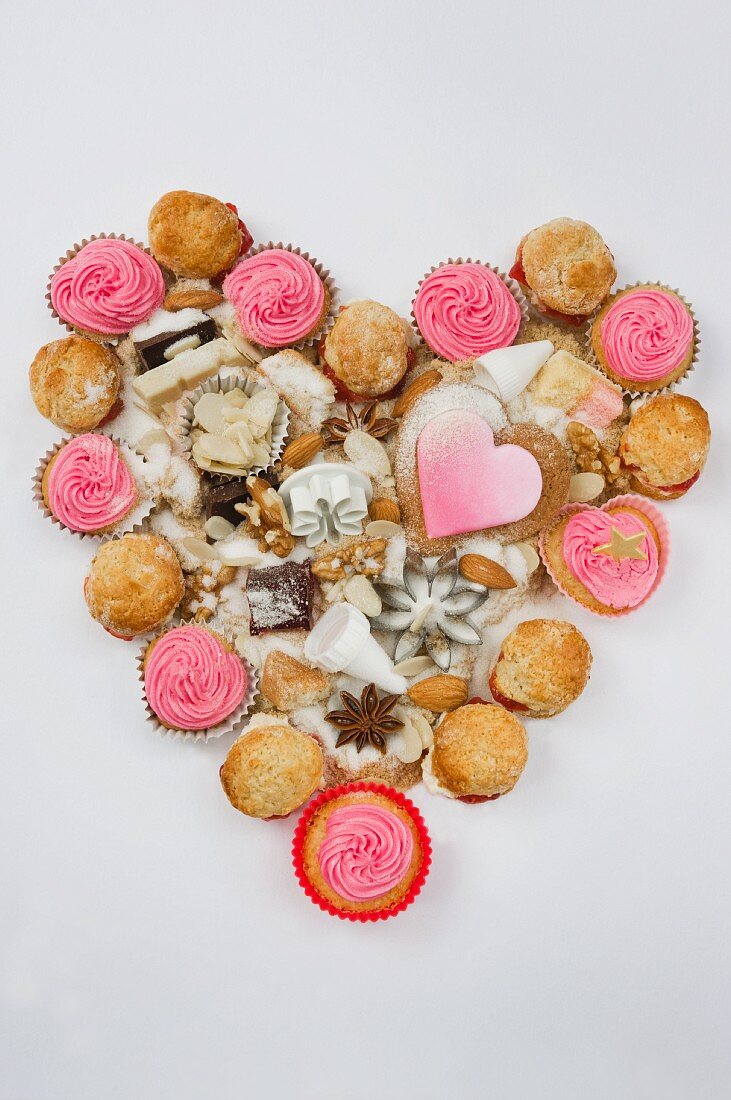 Cupcakes, biscuits, baking paraphernalia, chocolate and flour, arranged in a heart shape