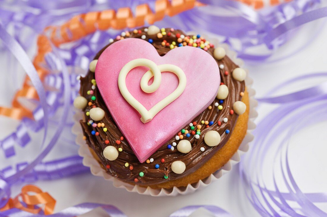 A cupcake decorated with chocolate icing and a pink heart between streamers