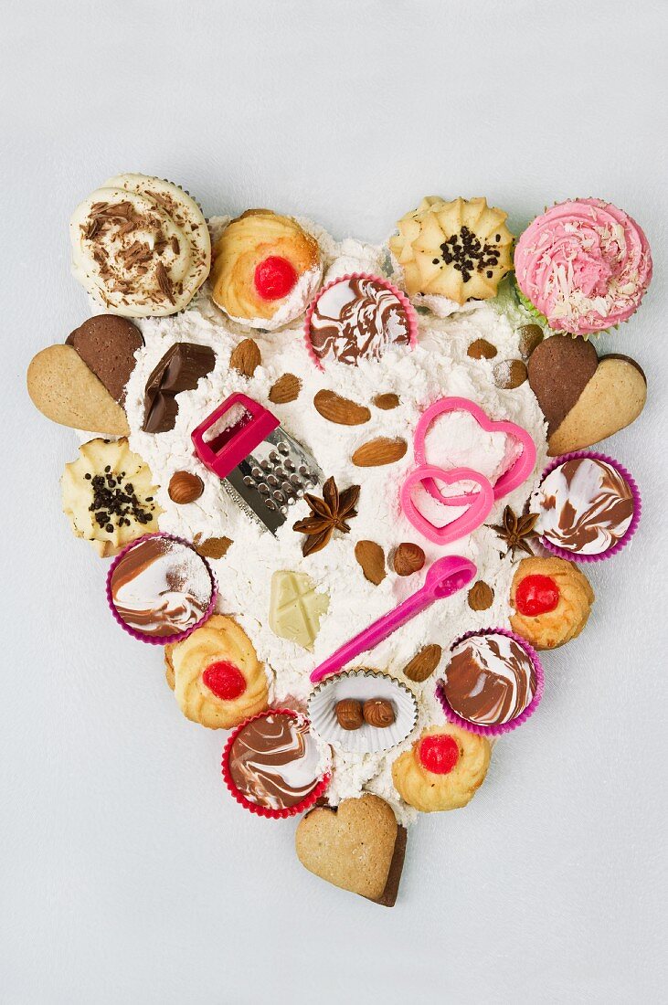 Cupcakes, Biscuits, Backutensilien, Schokolade und Mehl, arrangiert in Herzform