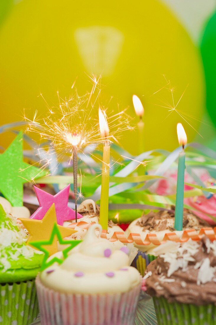 Party-Cupcakes mit brennenden Kerzen, Luftschlangen und Luftballons