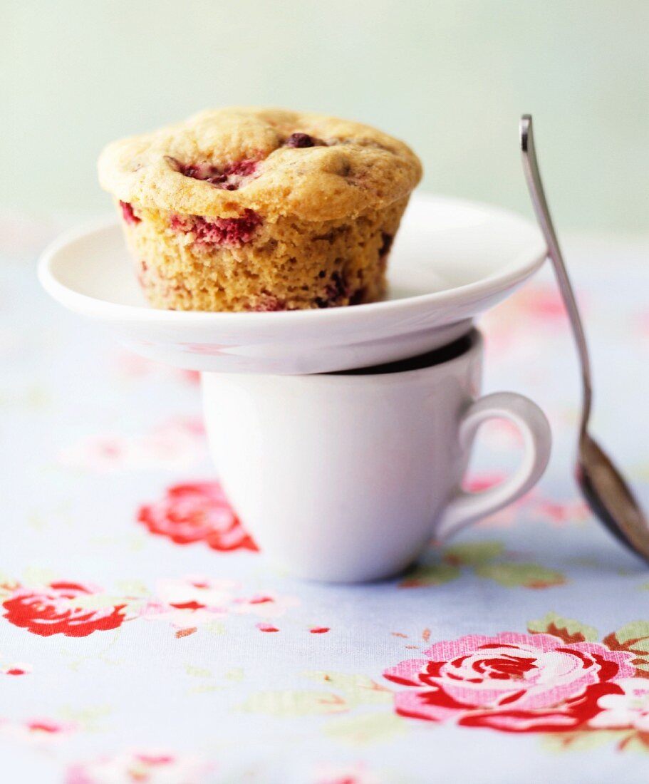 A plate with a cherry muffin on top of an espresso cup