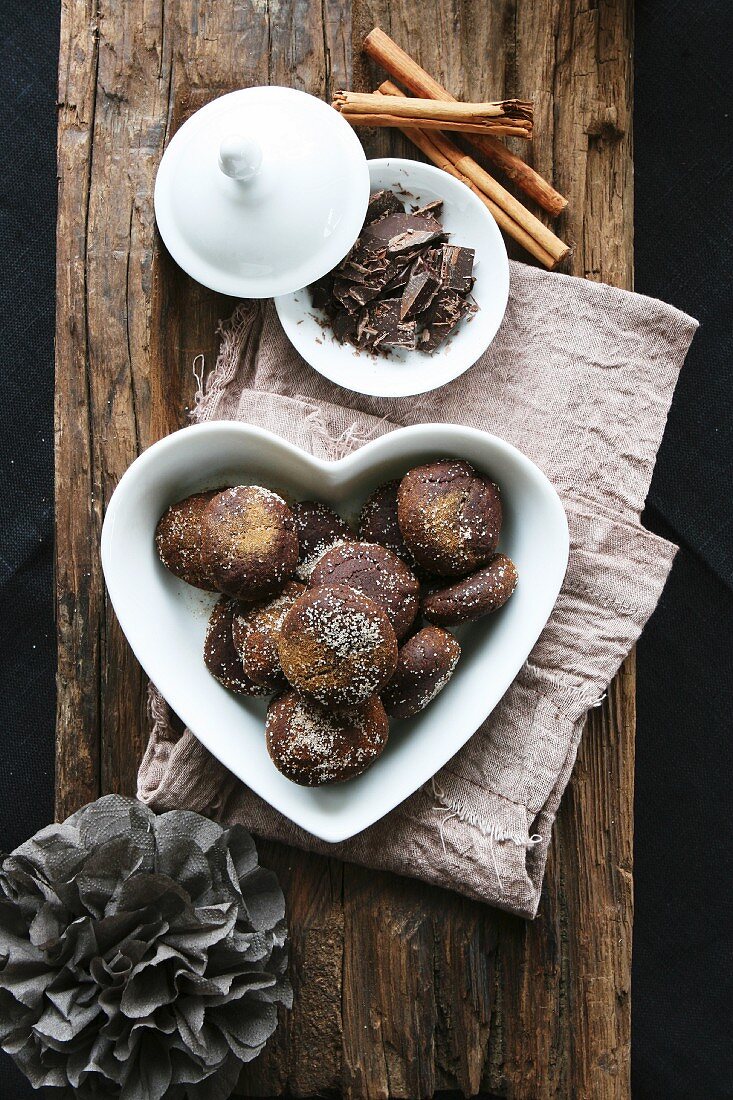 Chocolate and cinnamon treats in a heart-shaped bowl, grated chocolate, cinnamon sticks