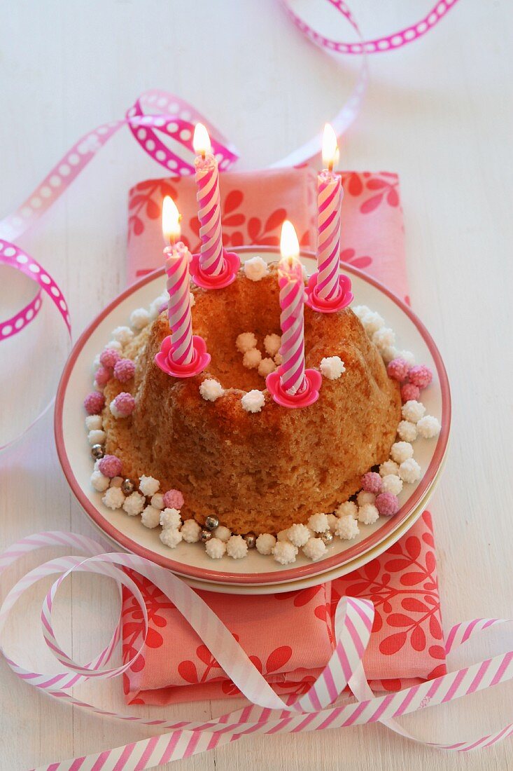 Kleiner Geburtstagskuchen mit brennenden Kerzen und Luftschlangen