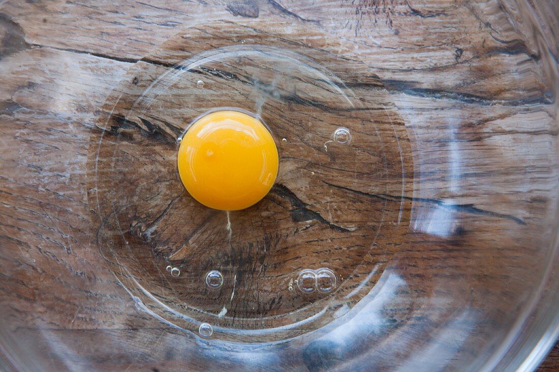 A raw egg in a glass bowl (view from above)