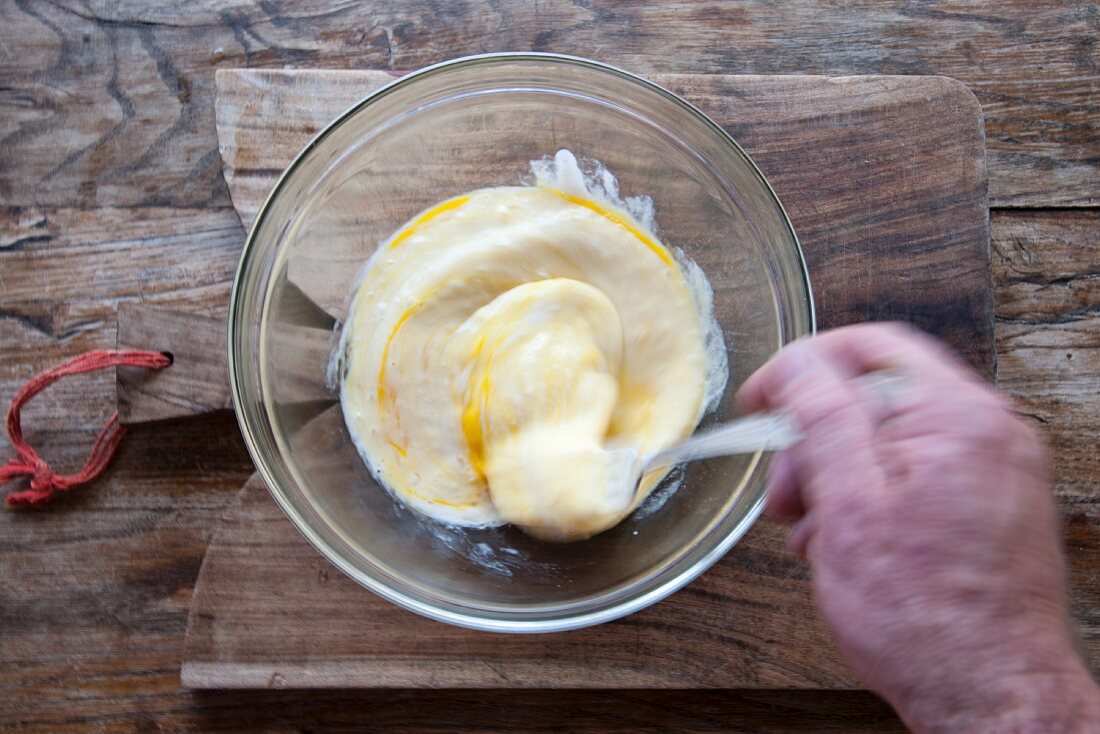 A hand beating eggs with a fork in a glass bowl