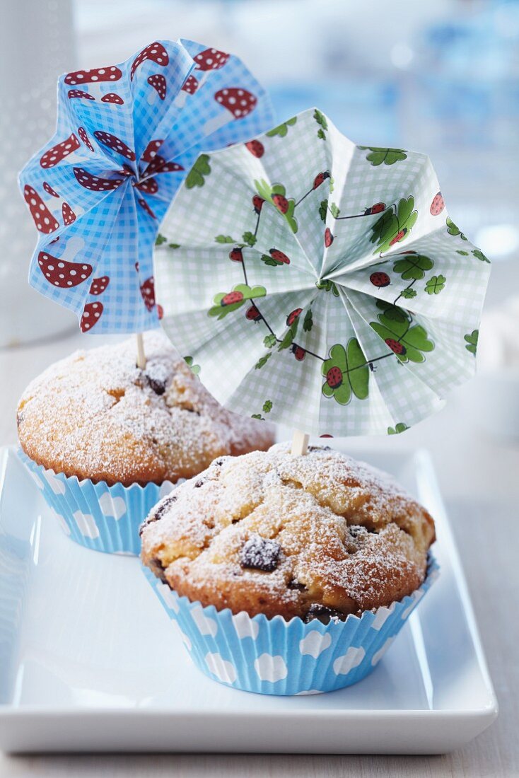 Colourful paper flowers attached to small wooden forks decorating muffins