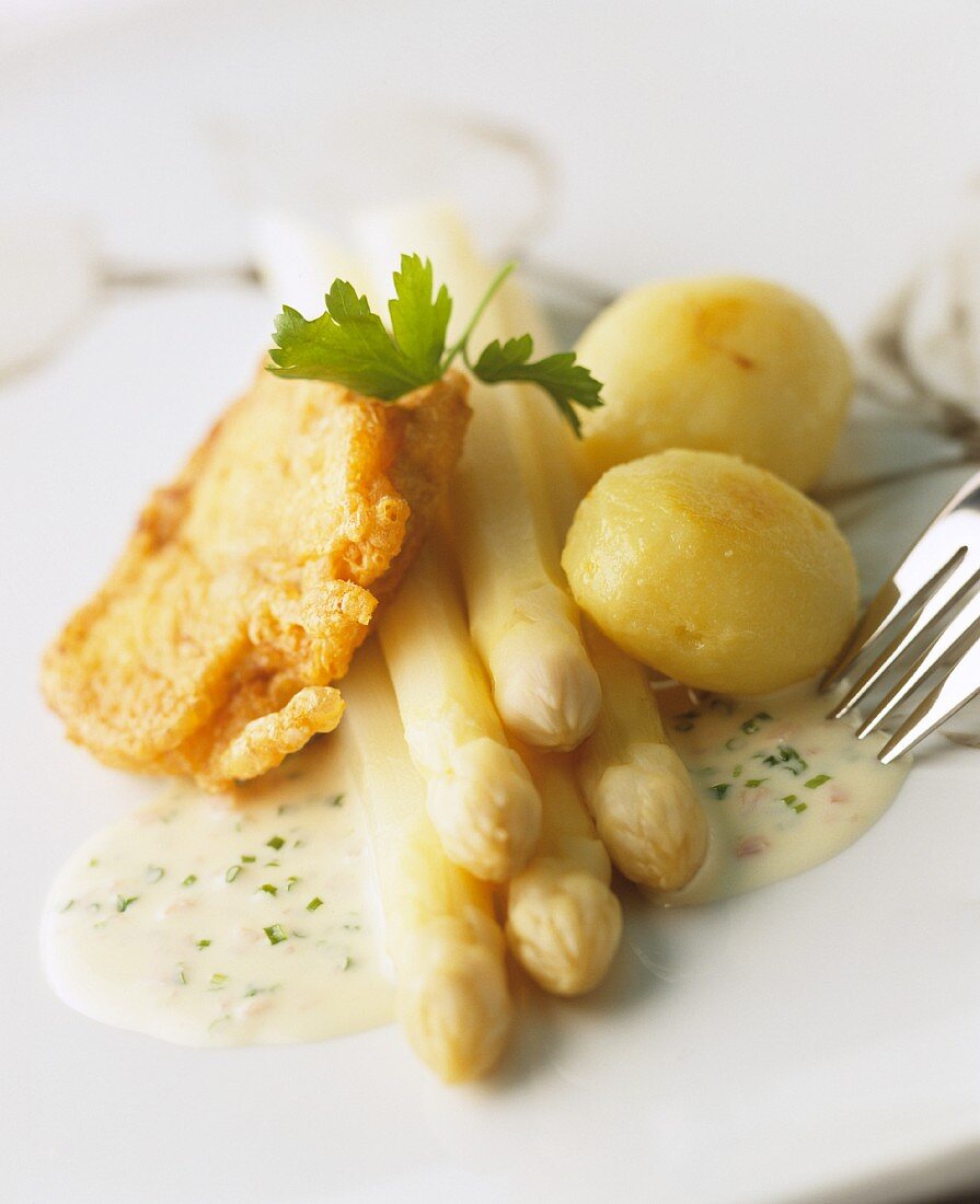 White asparagus with breaded fish fillet, potatoes and a herb sauce