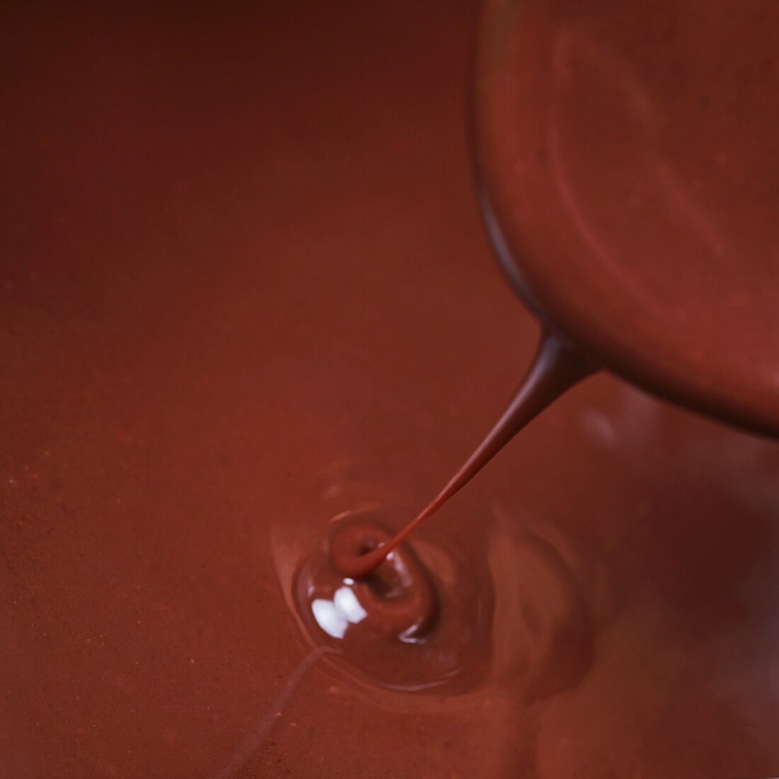 Schokoladensauce fliesst vom Löffel in einen heißen Topf