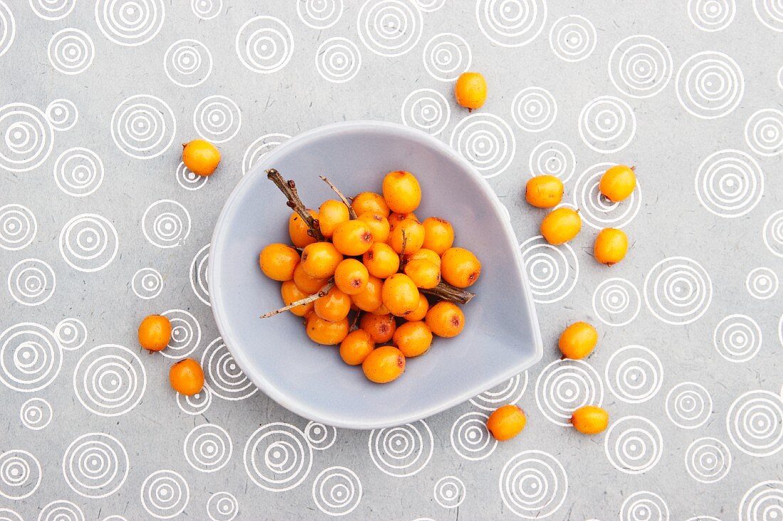 Sea buckthorn berries in a small bowl and on a tablecloth (view from above)