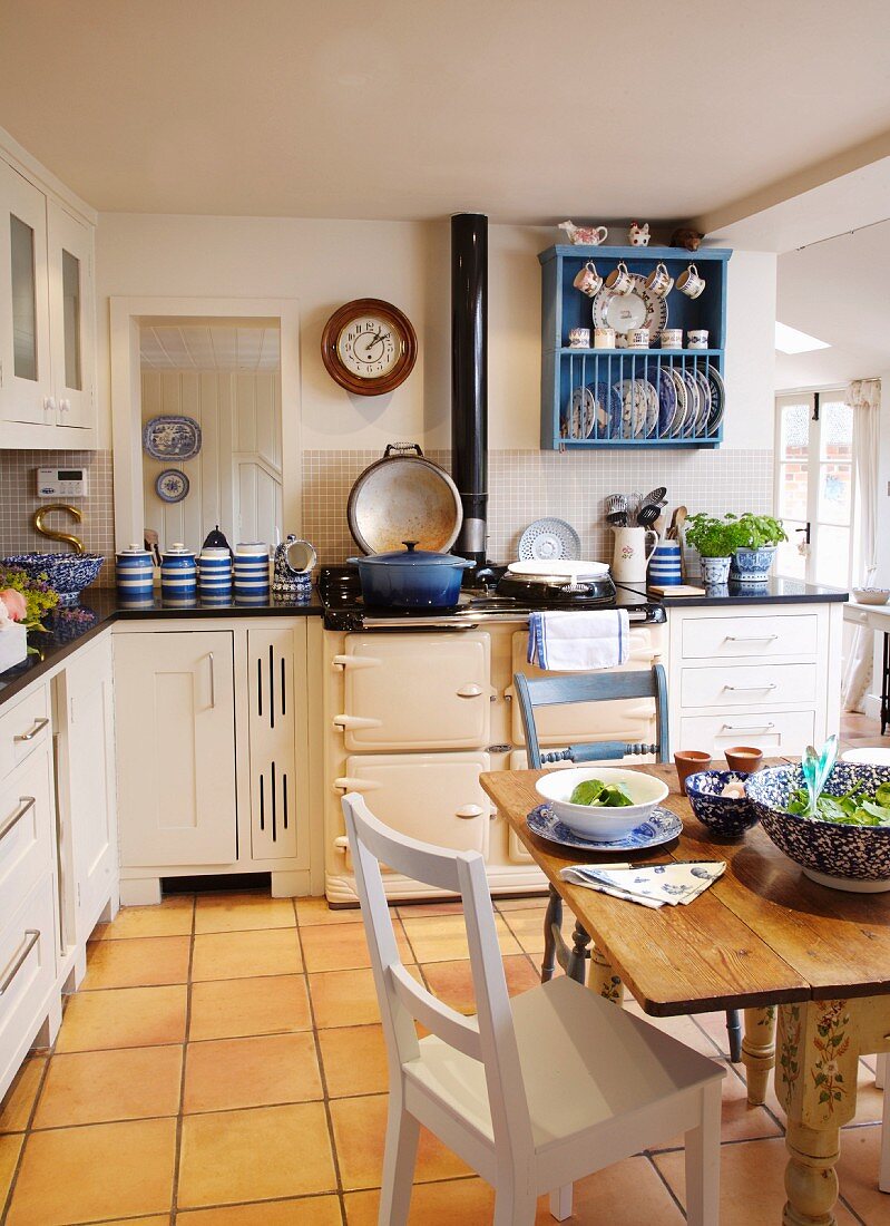 Rustikaler Esstisch mit Gedeck in weisser Landhausküche mit gelblichem Fliesenboden