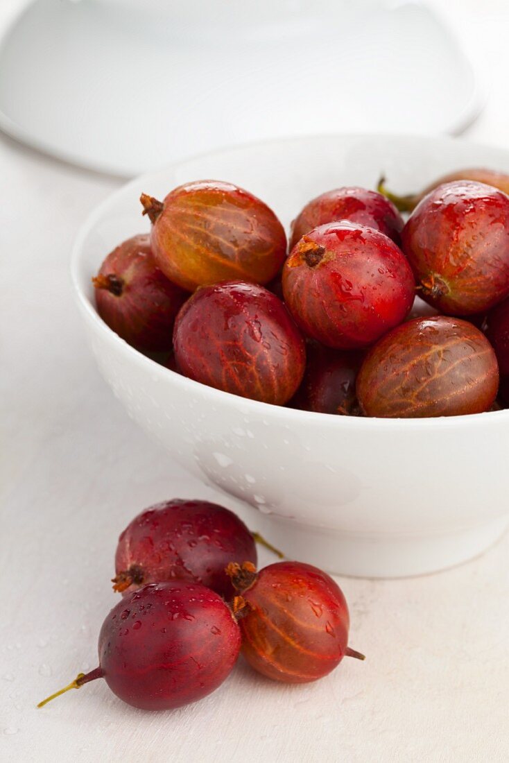 Rote Stachelbeeren in weisser Schale und davor