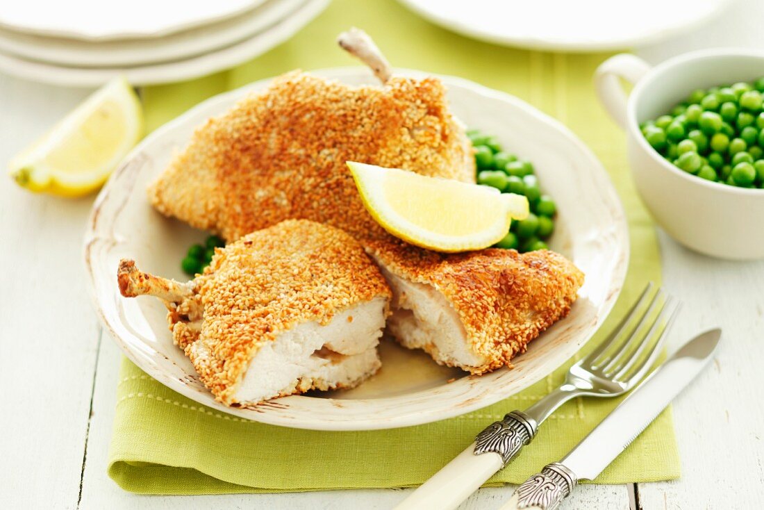 Breaded chicken escalope with butter, lemon wedges and peas